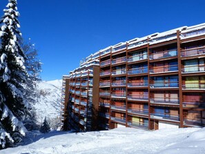 A multi-story hotel with balconies, surrounded by snow-covered trees and a clear blue sky. - 7th floor, view forest, tv, 13m², Les Arcs (Les Arcs)