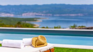 A poolside area with a straw hat and a towel on a lounge chair, overlooking a body of water and distant land. - Villa Mare - OneBedroom Villa with Pool (Vrbnik)