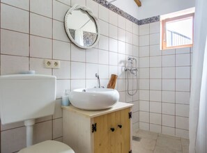 Un bagno con un lavandino bianco, un armadietto in legno e una doccia.
