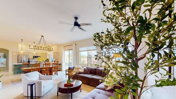 A spacious living room with a modern sofa, a coffee table, and a dining area with chairs and a chandelier. - Dog-friendly home with mountain views, ample outdoor space, & washer/dryer (Tucson)