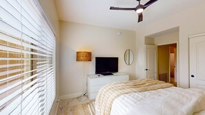 A bedroom with a bed, a television on a dresser, a ceiling fan, and a window with blinds. - Dog-friendly home with mountain views, ample outdoor space, & washer/dryer (Tucson)
