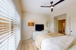 Ein Schlafzimmer mit einem Bett, einem Fernseher auf einer Kommode, einem Deckenventilator und einem Fenster mit Jalousien.