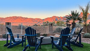 A patio with Adirondack chairs, a fire pit, and a view of red mountains. - Dog-friendly home with mountain views, ample outdoor space, & washer/dryer (Tucson)