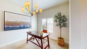 A dining area with a wooden table, a chandelier, a large abstract painting, a potted plant, and a window with blinds. - Dog-friendly home with mountain views, ample outdoor space, & washer/dryer (Tucson)