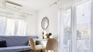 A modern living room with a grey sofa, two wicker chairs, a small table with a wine glass and fruit, and a large window with sheer curtains. - Monika Seaside Apartment - OneBedroom Apartment With Balcony (Kastel Luksic)