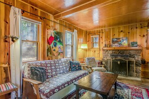 Interior acogedor de una cabaña con detalles de madera, un sofá con cojines estampados, una chimenea y obras de arte en las paredes.