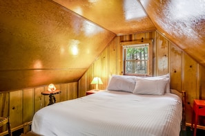 Un dormitorio abrigado en el ático con una cama grande, una ventana y paredes de madera.