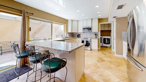 A modern kitchen with a central island, bar stools, built-in appliances, and a view to the outside. - Gorgeous home with private pool, grill, games, near golf (Scottsdale)