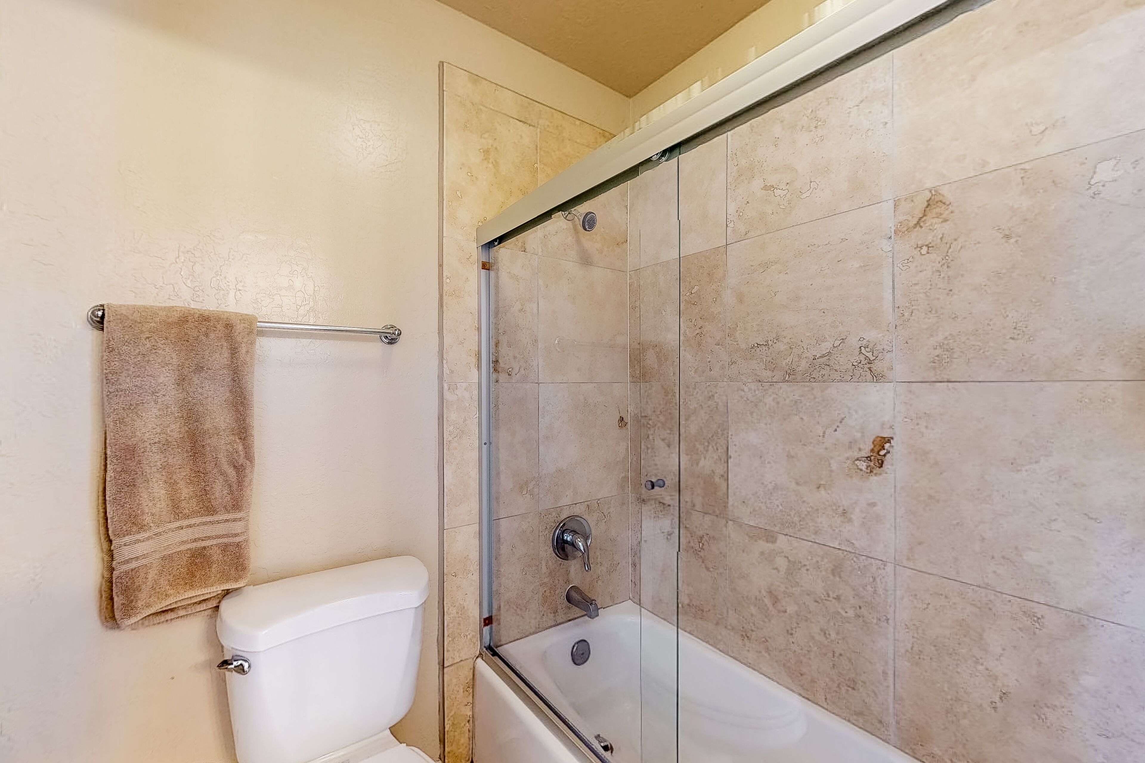 Een badkamer met toilet, een douchecabine van glas en beige betegelde wanden.