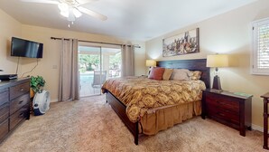 A bedroom with a bed, a ceiling fan, a TV, a nightstand, and a window with curtains. - Gorgeous home with private pool, grill, games, near golf (Scottsdale)