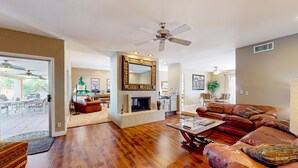 A spacious living room with hardwood flooring, a fireplace, a ceiling fan, and a large mirror. - Gorgeous home with private pool, grill, games, near golf (Scottsdale)