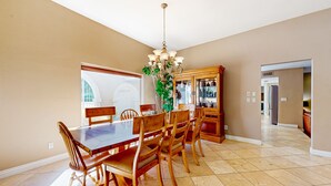 A dining area with a large wooden table, six chairs, a chandelier, and a cabinet with glass doors. - Gorgeous home with private pool, grill, games, near golf (Scottsdale)