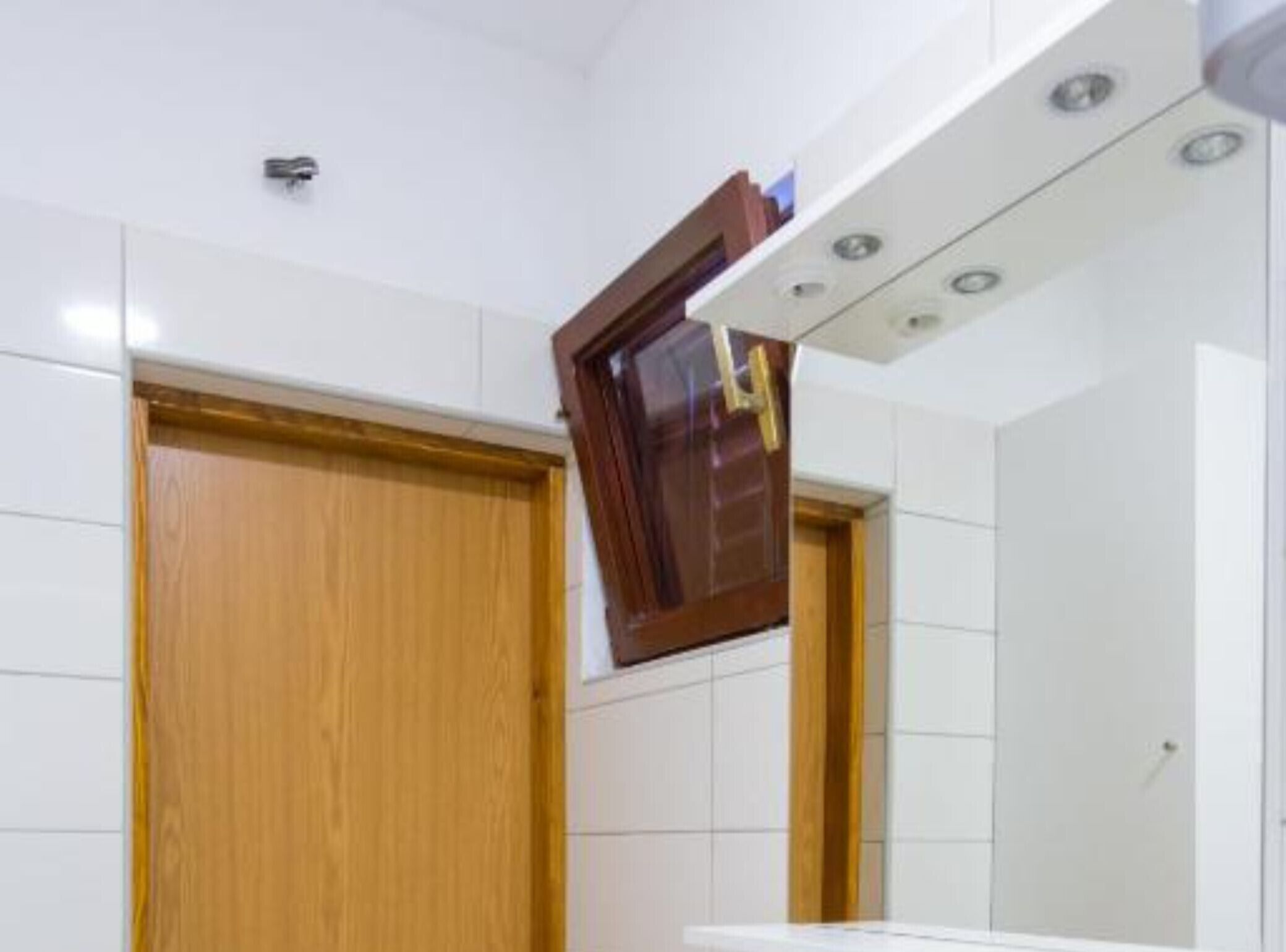 Un baño con paredes de azulejos blancos, una puerta de madera y un espejo.