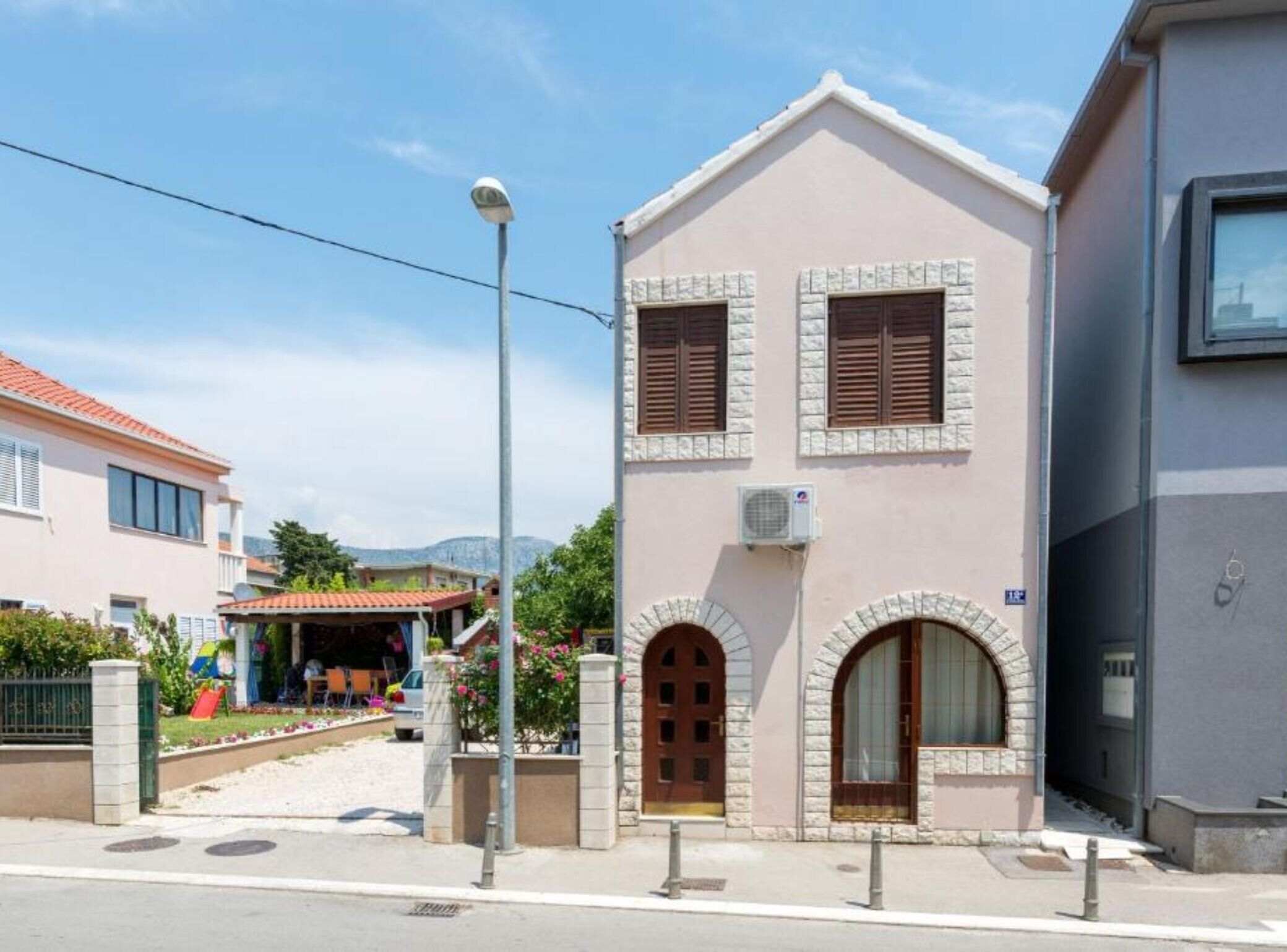 Un edificio de dos pisos con fachada de piedra, una entrada central con puerta de madera y un pequeño porche con techo rojo.