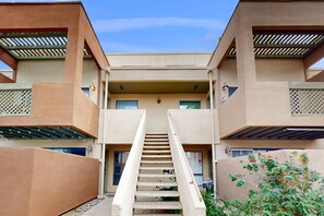 Ein Gebäude mit einer zentralen Treppe, die zu einer oberen Ebene führt, umgeben von beigen Wänden und einem überdachten Gang.