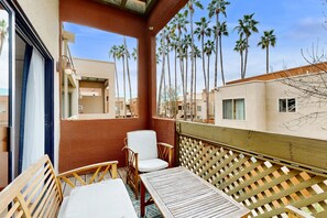 A balcony with a wooden table and chairs, overlooking a row of palm trees and adjacent buildings. - Bright condo with pool, hot tub, gym & ideal downtown Scottsdale location (Scottsdale)