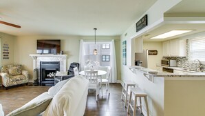 Ein Wohnzimmer mit Kamin, ein Essbereich mit Tisch und Stühlen sowie eine Küche mit Arbeitsfläche und Geräten.
