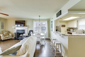Ein Wohnzimmer mit Kamin, ein Essbereich mit Tisch und Stühlen sowie eine Küche mit Arbeitsfläche und Geräten.