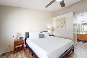 Ein Schlafzimmer mit Bett, Nachttisch, Wandbild und Deckenventilator.