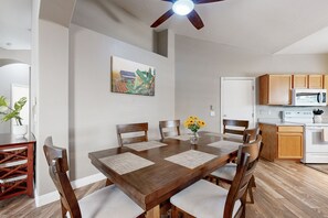 A dining area with a wooden table, four chairs, a ceiling fan, a white refrigerator, wooden cabinets, and a microwave. - Modern home with large yard, mountain views, & convenient location (Phoenix)