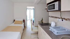 Een kleine hotelkamer met twee bedden, een kitchenette en uitzicht op buiten.