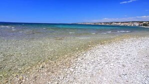 Een kiezelstrand met helder water en een stad in de verte.
