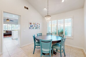 A dining area with a round table, teal chairs, a chandelier, and a window with blinds. - Dog-friendly desert retreat with lovely pool & spa - minutes to Tennis Garden (Palm Desert)