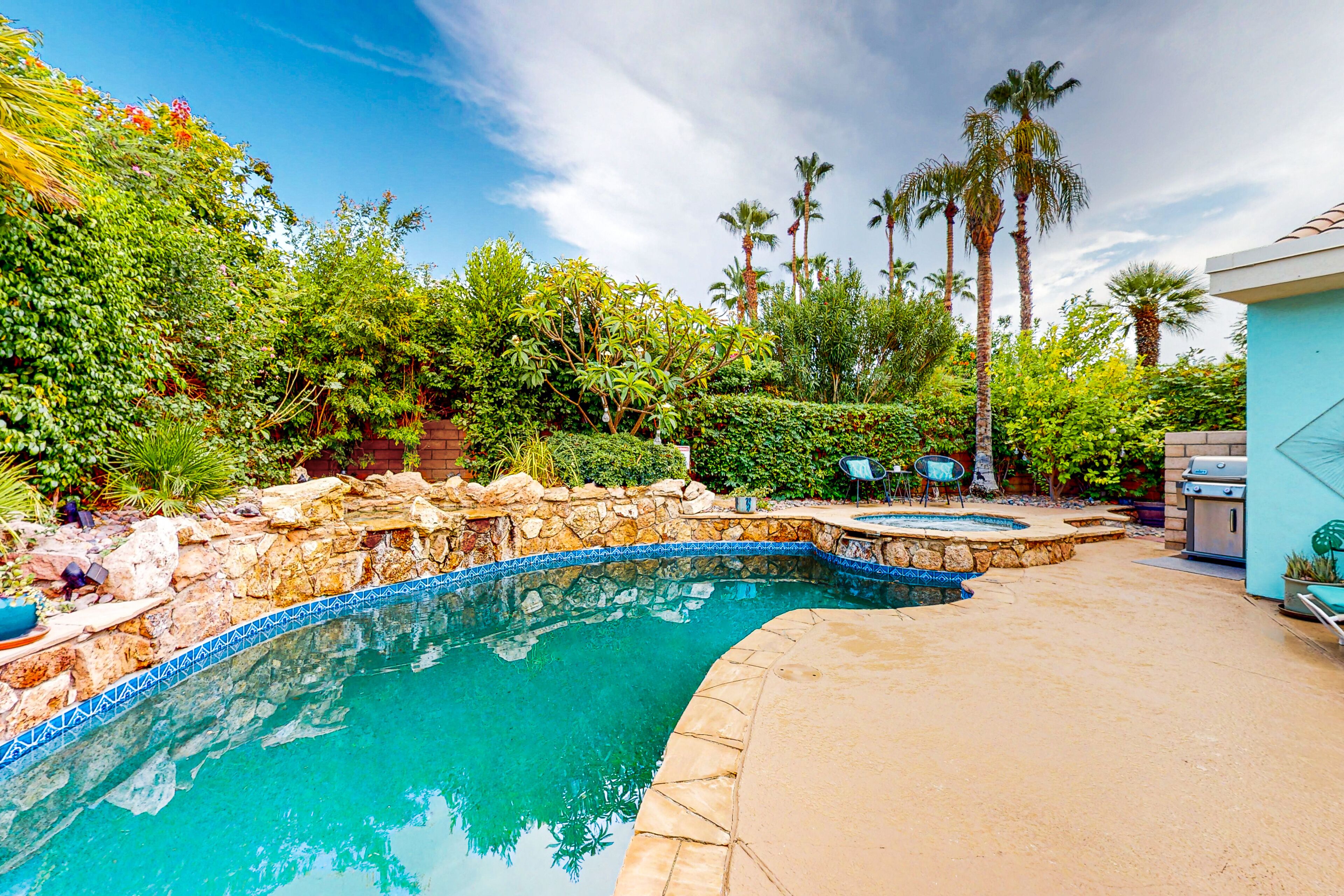 Una piscina con borde de piedra, rodeada de exuberante vegetación y palmeras.