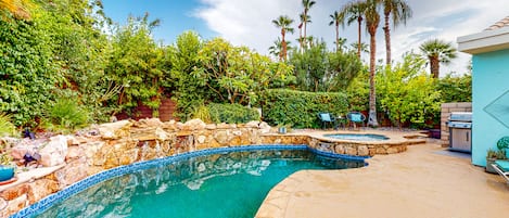 Una piscina con borde de piedra, rodeada de exuberante vegetación y palmeras.