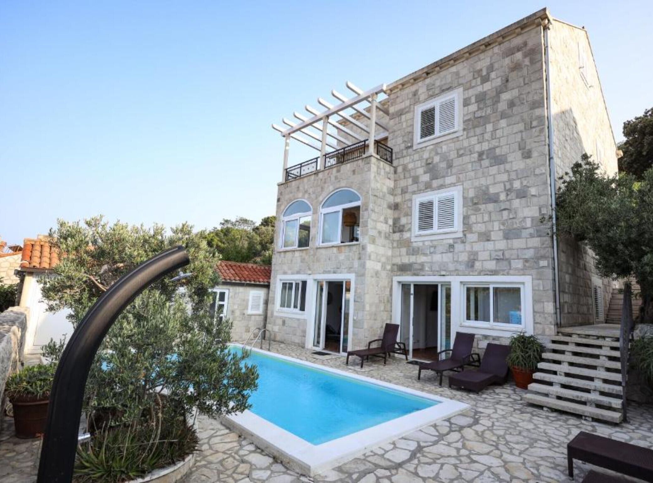 A stone building with a pool, outdoor seating, and a pergola.