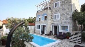 Ein Steinhaus mit Pool, Sitzgelegenheiten im Freien und einer Pergola.