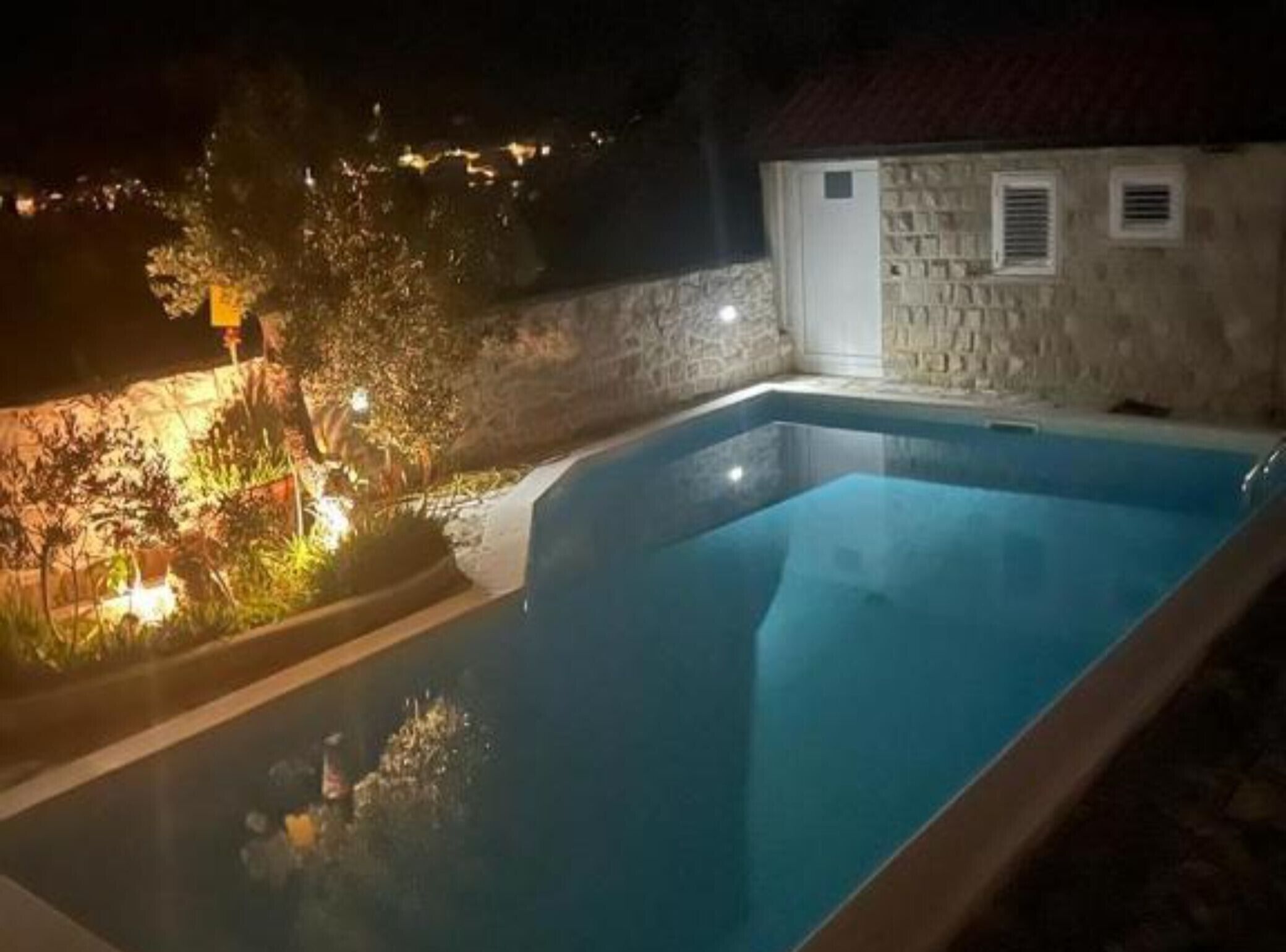 A swimming pool with a stone wall and a small building with a red roof.