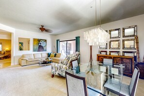 A spacious living room with a sofa, a glass coffee table, and a dining area with chairs and a chandelier. - Second-floor condo with heated pool, hot tub, balcony, central AC & washer/dryer (Scottsdale)