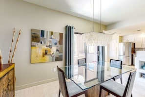 A modern dining area with a glass table and chairs, a contemporary painting, and a kitchen in the background. - Second-floor condo with heated pool, hot tub, balcony, central AC & washer/dryer (Scottsdale)
