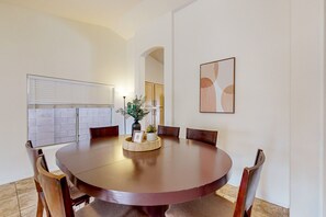 Une table de salle à manger ronde, entourée de six chaises, un vase rempli de fleurs et un tableau encadré posé sur la table.