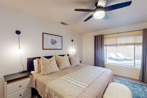 A bedroom with a bed, bedside tables, a ceiling fan, a window with curtains, and a framed picture on the wall.