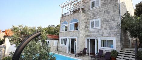 A stone building with a pool, outdoor seating, and a pergola.