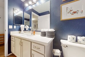 A bathroom with a white sink, a mirror, a toilet, and a framed artwork on the wall. - Modern ground-level townhome with two screened patios, grill, pool & hot tub (Scottsdale)