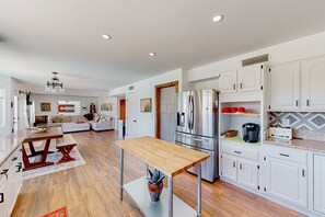 A modern kitchen with white cabinets, stainless steel appliances, and a wooden dining table. - Golf-course-front home with private pool, spa, terrace & mountain view (Oro Valley)
