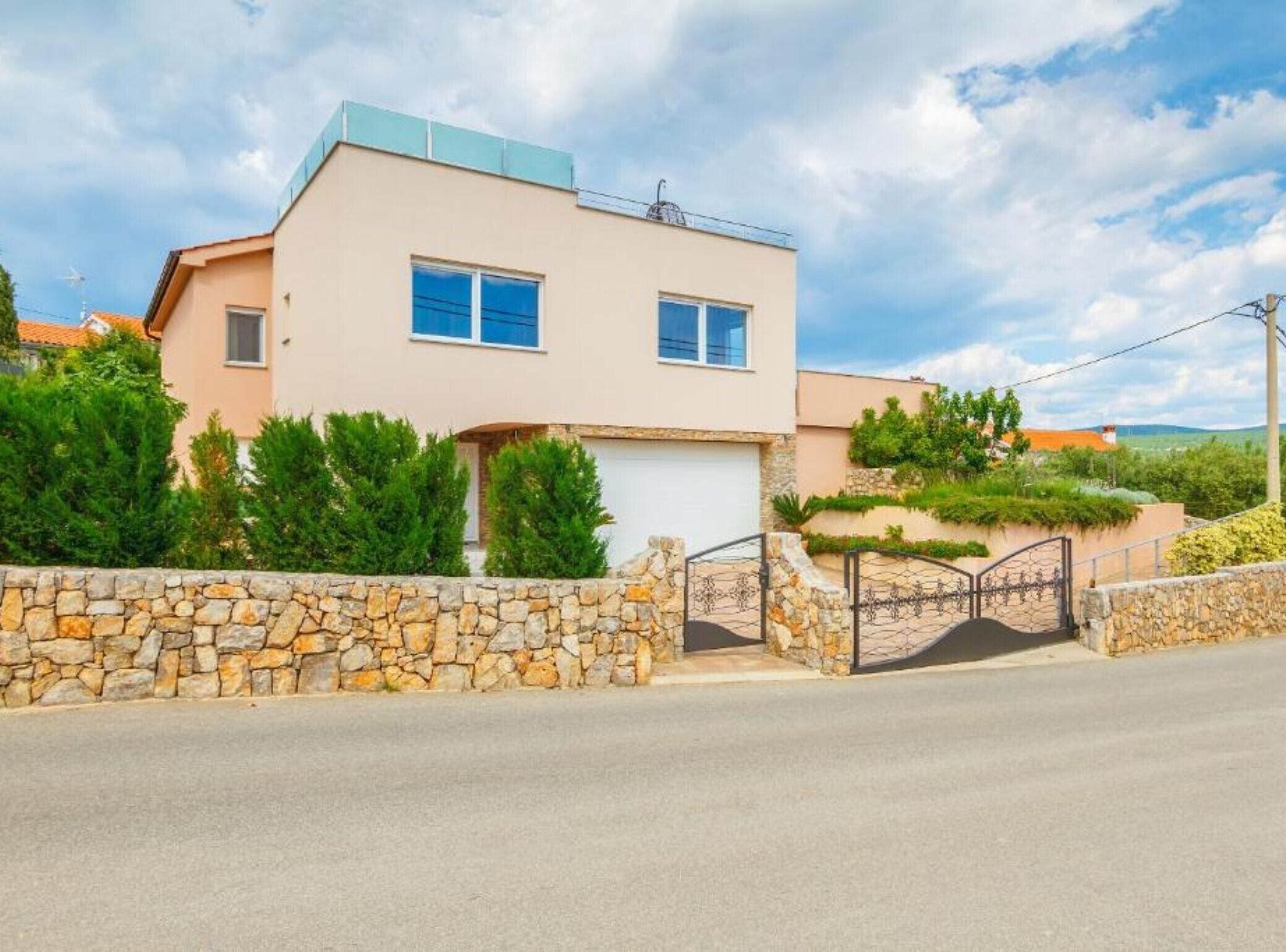 A modern two-story house with a stone wall entrance, a garage, and a clear sky.