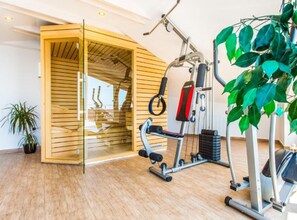 Ein modernes Fitnessstudio mit Holzwand und Glastür, ausgestattet mit verschiedenen Trainingsgeräten und einer großen Topfpflanze.
