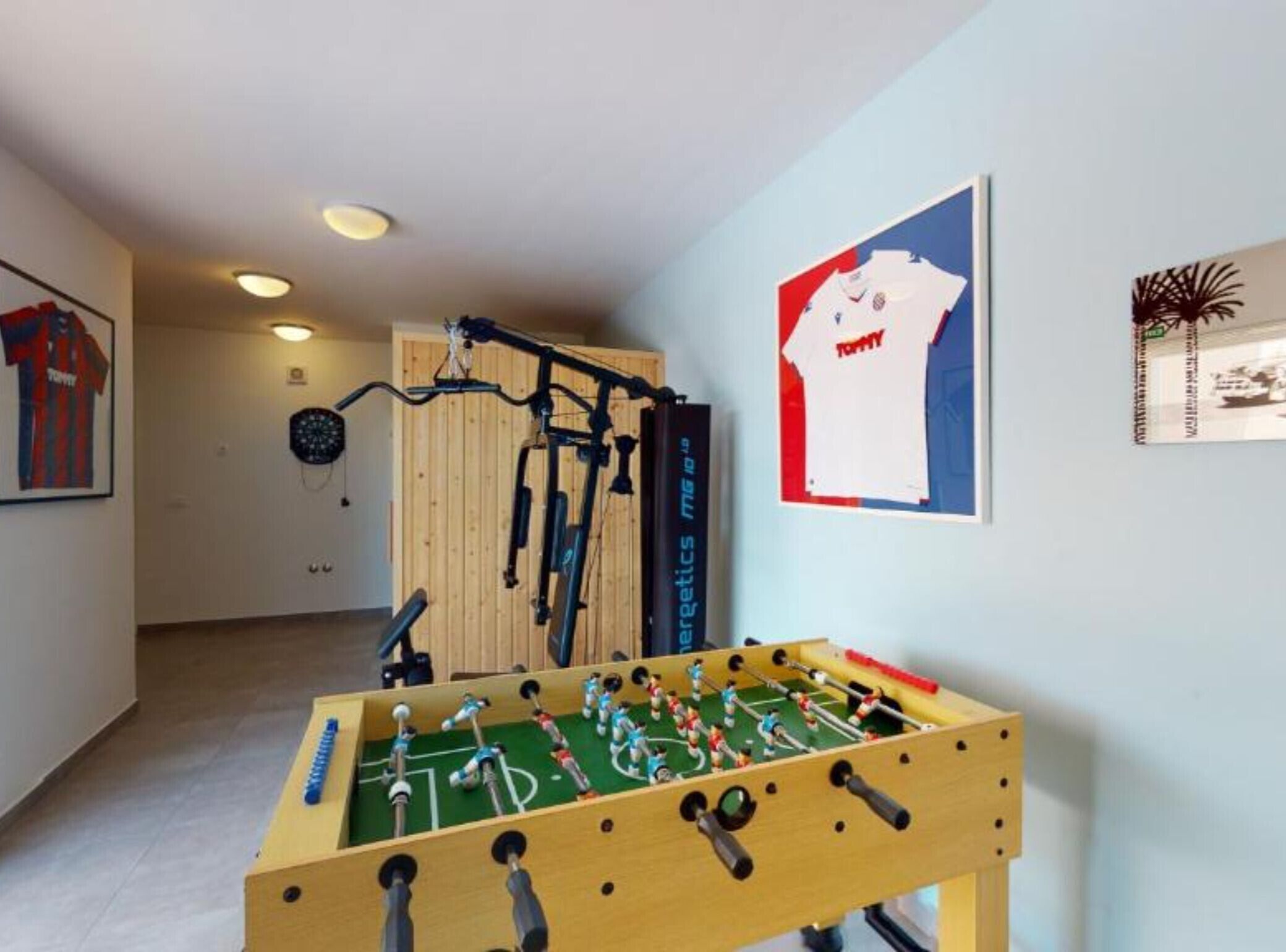 Ein Zimmer mit einer Kicker-Tischfußballanlage, Fitnessgeräten und Sportmemorabilien an den Wänden.