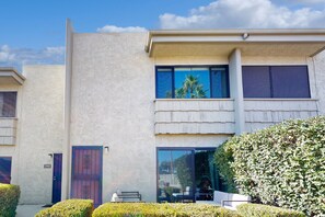 A two-story building with a beige exterior, a blue door, and a large window reflecting palm trees. - Fully remodeled condo near Fashion Square with pool, fireplace, patio, streaming (Scottsdale)