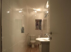 A small, compact bathroom with white tiles, a toilet, a sink, and a window.