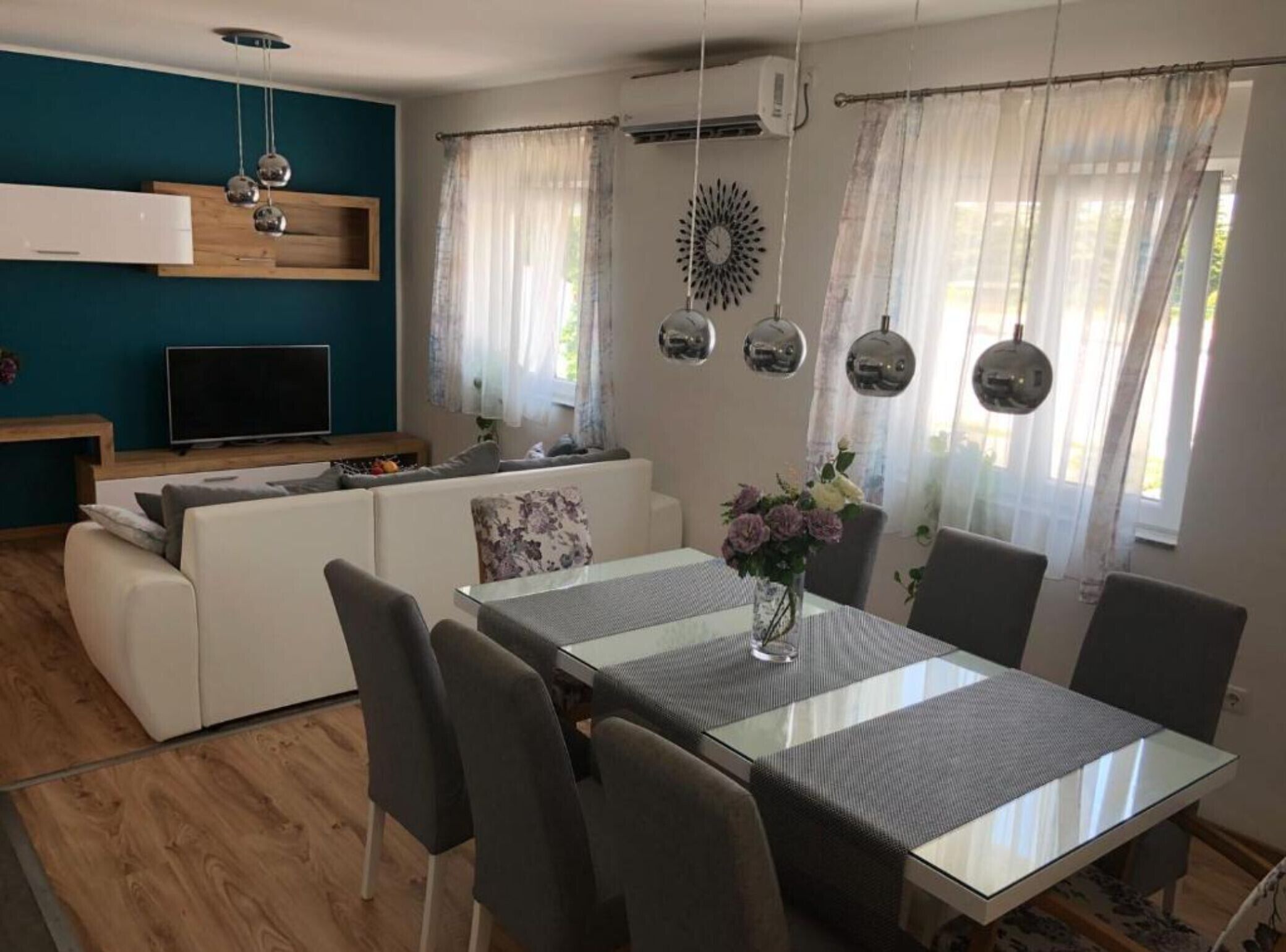 Un salon moderne comprenant un coin repas, un ensemble de canapés, un téléviseur et des miroirs décoratifs.