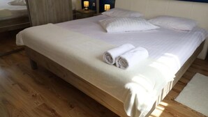 Un lit bien fait, avec du linge de lit blanc et des serviettes pliées, un plancher en bois et une table de chevet avec une lampe.