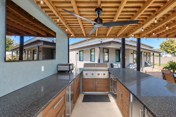 An outdoor kitchen area with a built-in grill, wooden cabinets, and a ceiling fan. - Charming Chandler retreat with pool, guest house, pickleball and putting green! (Chandler)