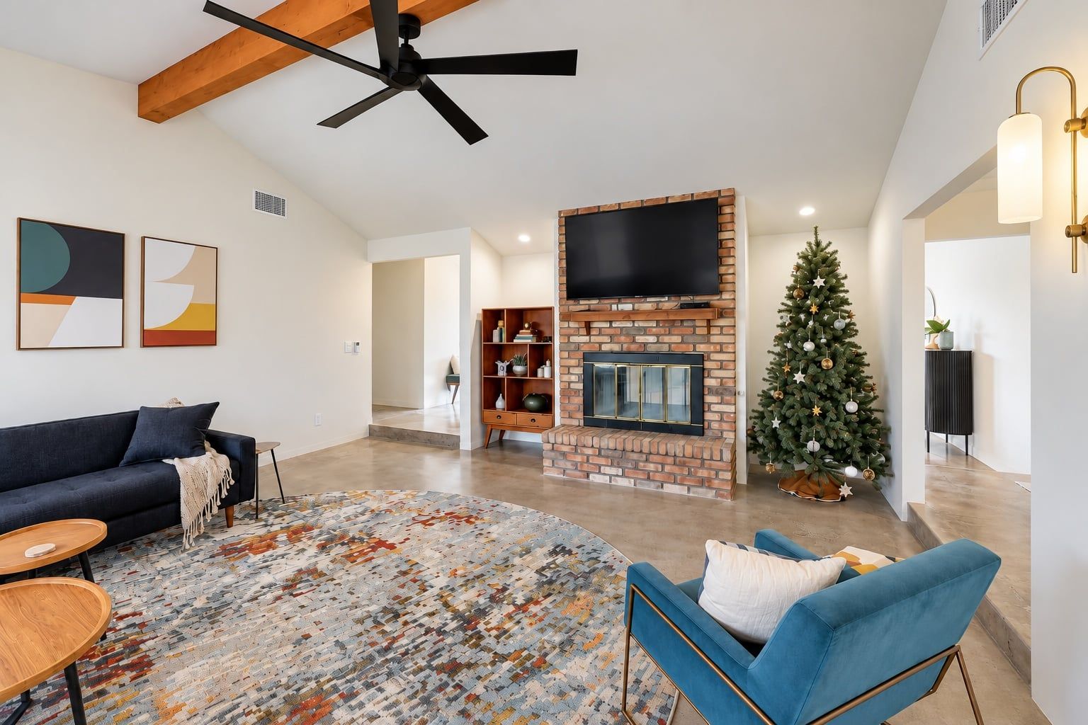 A modern living room with a fireplace, a ceiling fan, and a Christmas tree.
