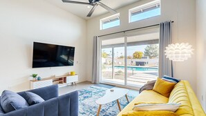 Ein modernes Wohnzimmer mit einem Flachbildfernseher, einem gelben Sofa, einem blauen Sessel und einem Couchtisch.