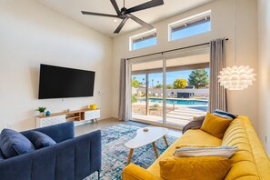 A modern living room with a flat-screen TV, a sofa, a coffee table, and a view of a swimming pool through large glass doors.